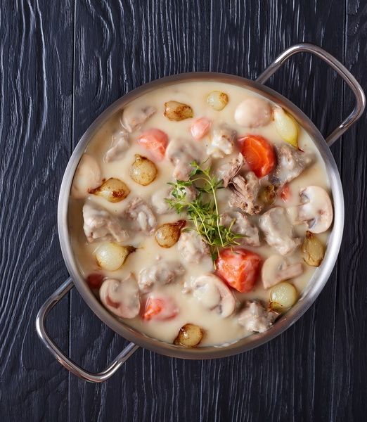creamy veal stew or blanquette de veau - pieces of veal meat stewed with mushrooms glazed pearl onions, and vegetables in casserole, authentic french recipe, view from above